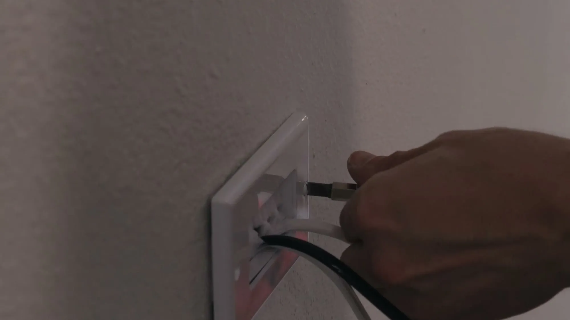 Cable pulled through a recessed in-wall power outlet behind a mounted TV